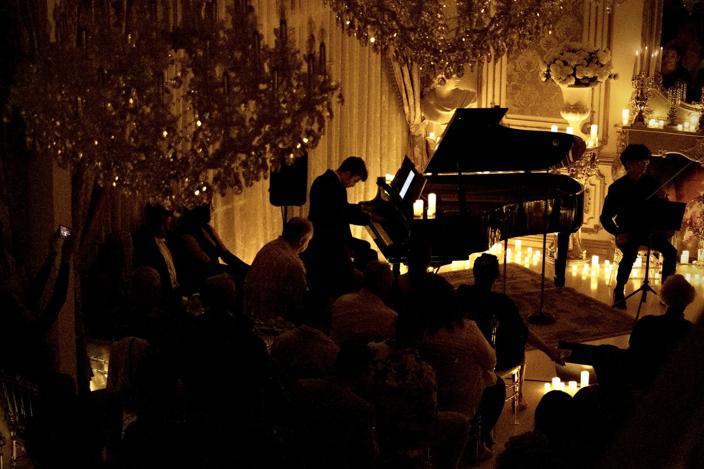 Evan Read at a grand piano during a candlelit concert, playing to a seated audience.