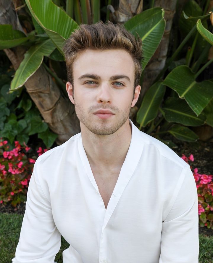Portrait of Evan Read in a white shirt, outdoors in front of tropical foliage.